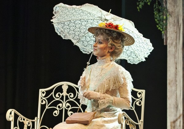 A lady in period clothing sitting on a garden bench holding a parasol
